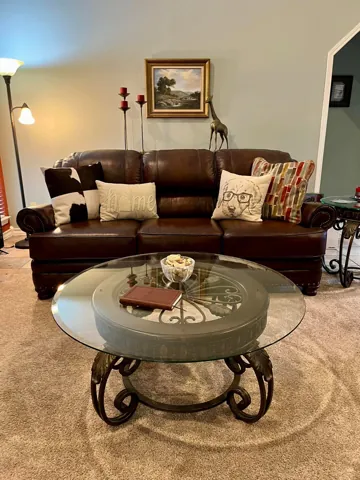 A brown leather sofa, patterned cushions, and a round glass table