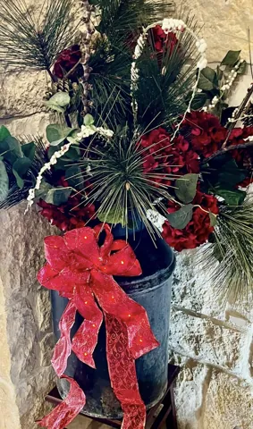 A stone-wall holiday arrangement with a lantern, berries, and red ribbon