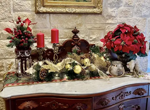 A decorated sideboard with candles, greenery, and red poinsettias