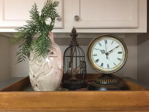 A white vase with greenery beside a decorative birdcage and clock